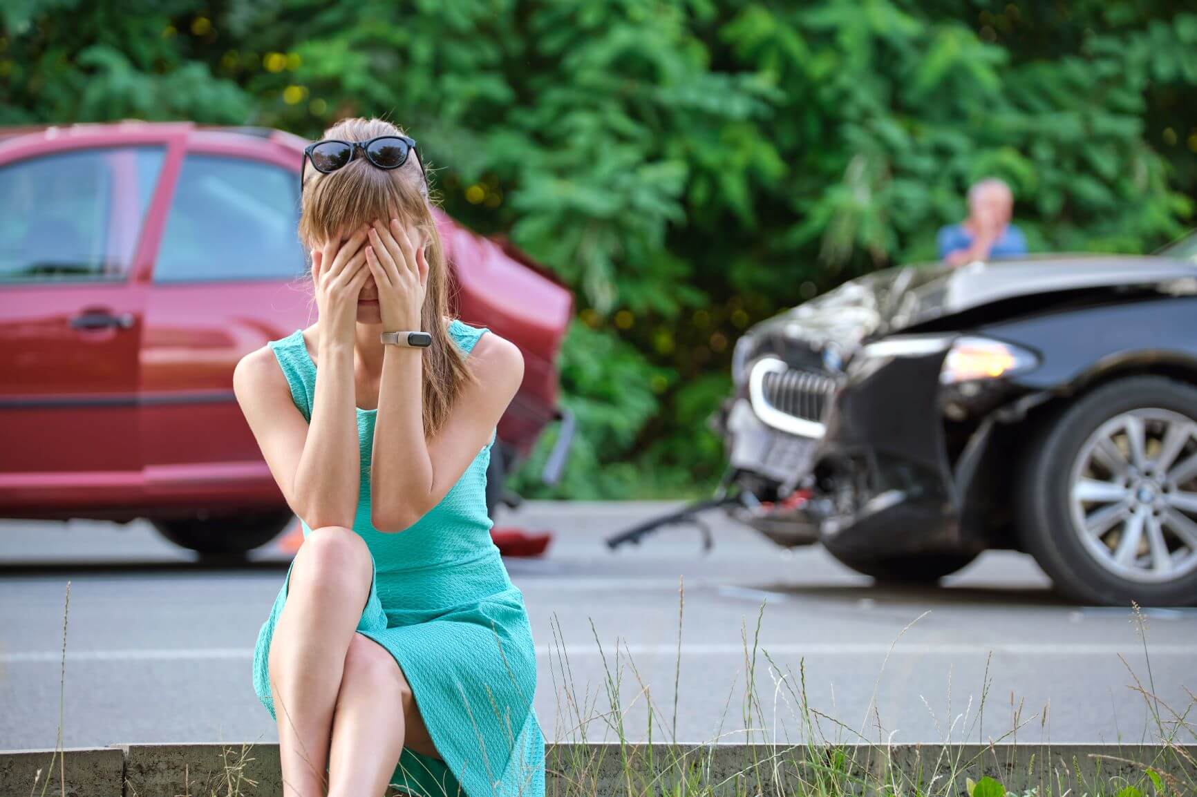 Shocked woman standing by her damaged car after an accident in California, expressing disbelief and distress.